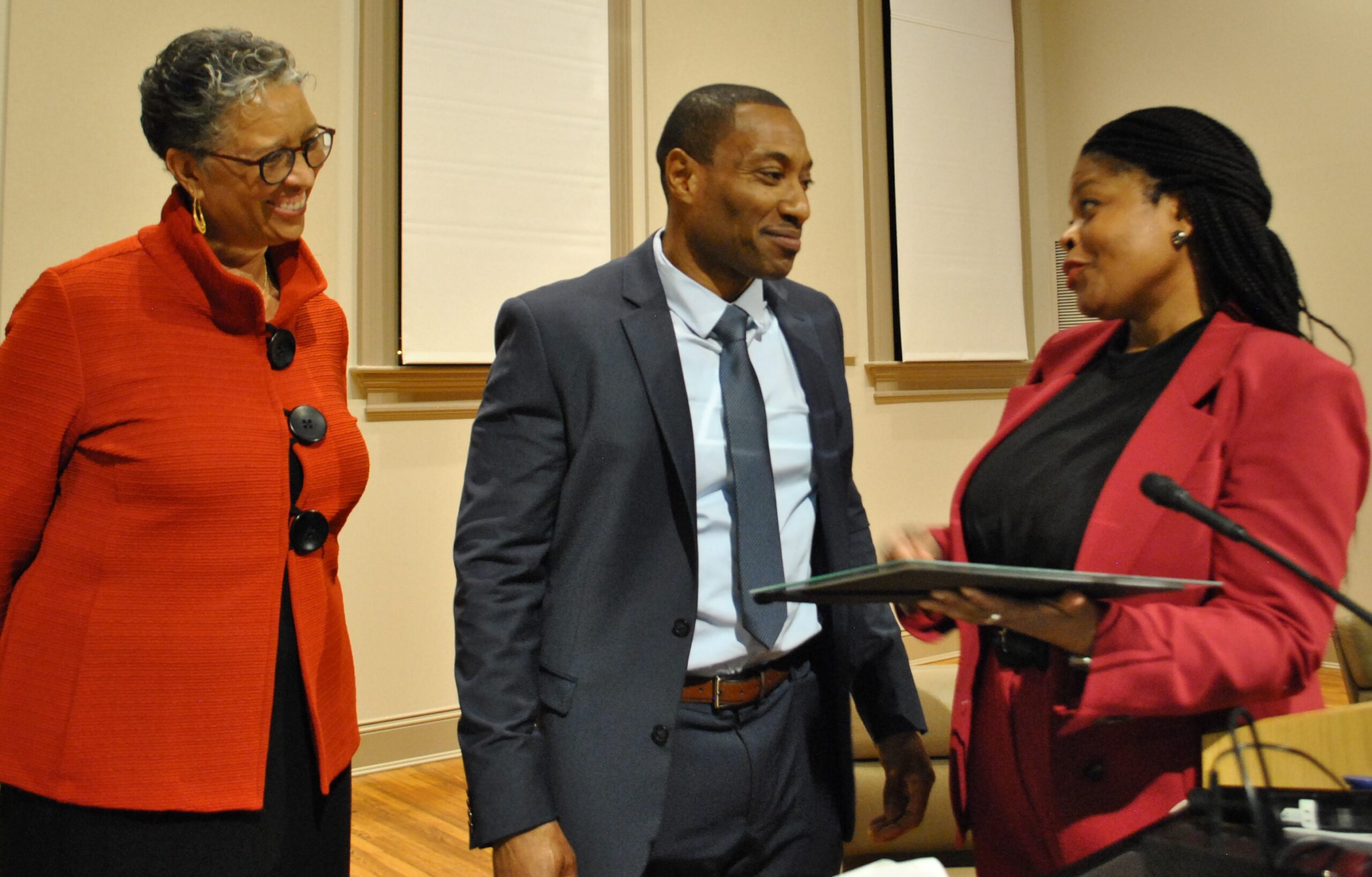 Recent graduate from Training Our Voices dressed in a suit smiling with staff members